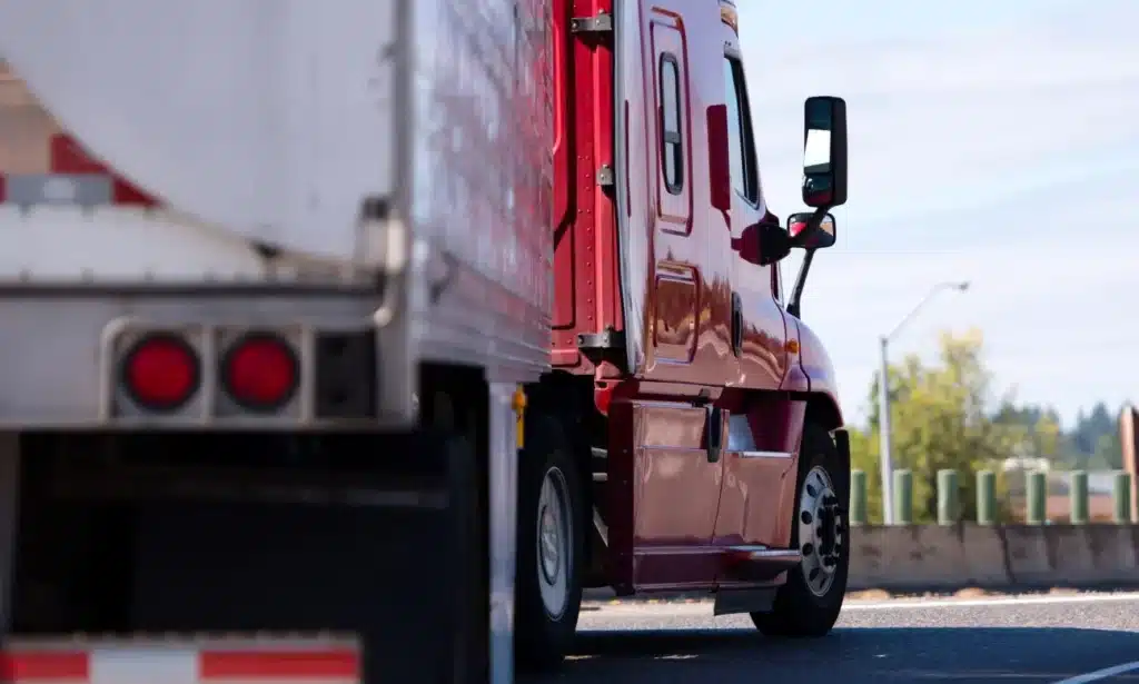 A red semi truck moving quickly toward a curve on a highway in the afternoon.