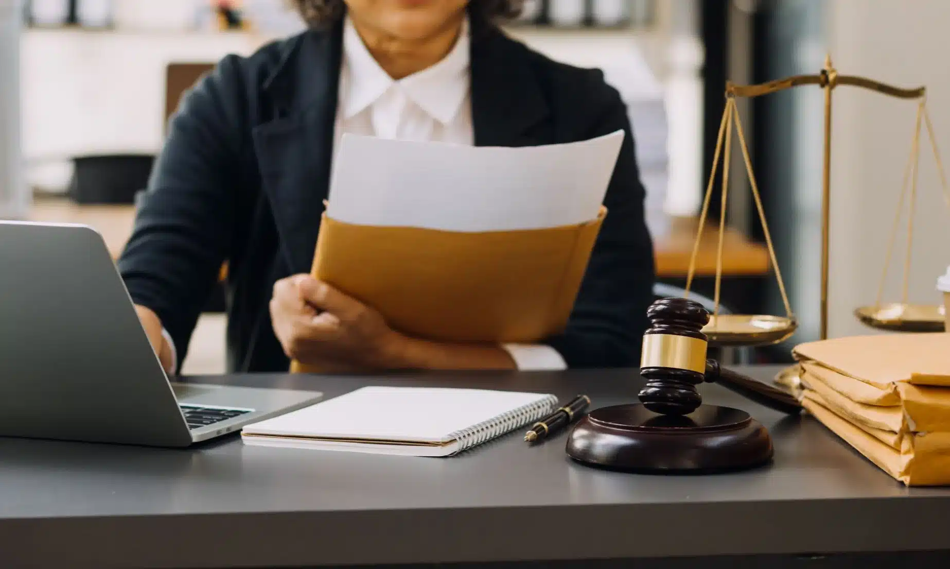 A lawyer with a folder full of documents working on her client's case on a laptop.