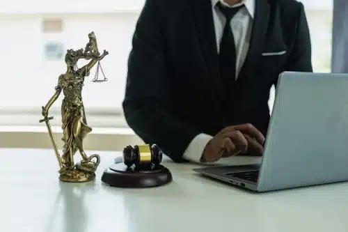 A personal injury lawyer typing on a laptop next to a statue of Lady Justice on a desk.