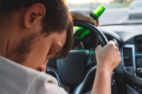 A drunk driver asleep at the wheel with a bottle in hand in the middle of traffic.