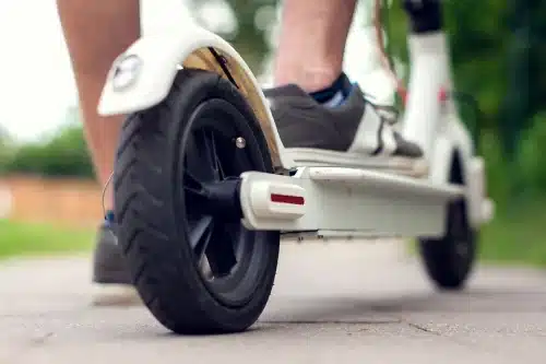 A closeup of an electric scooter and the feet of a person riding it.