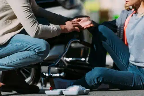 A motorcyclist helping up a woman who was hit by their motorcycle in a daytime accident.