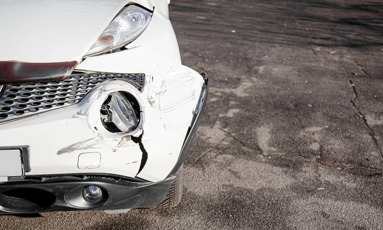 A partial view of a white car's damaged front end after an accident.