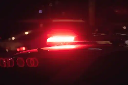 A police car with a flashing red light responding to the scene of a car accident at night.