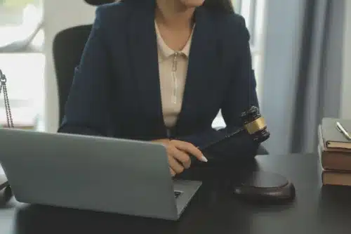 A lawyer holding a gavel in her hand with arms crossed behind a desk.
