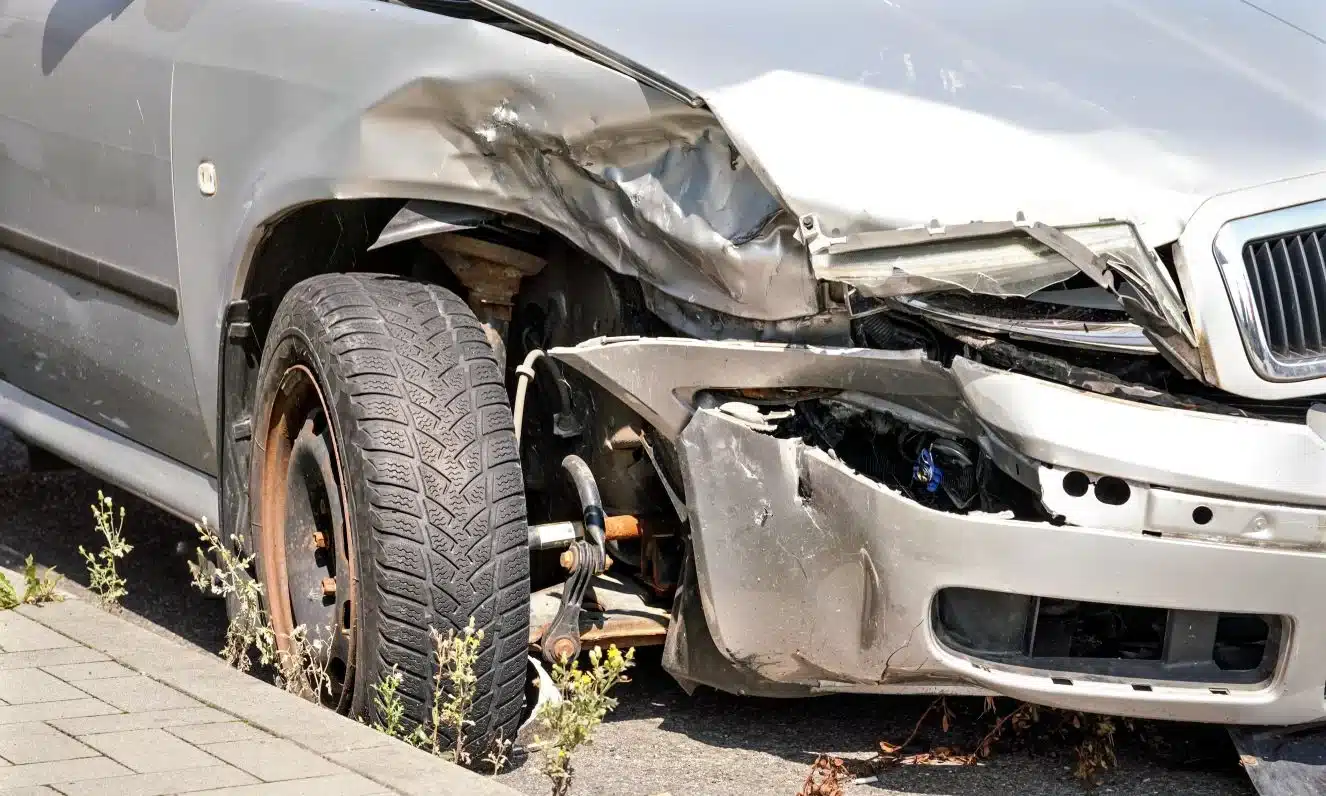 A grey car on the side of the road after receiving damage to its bumper in an accident.
