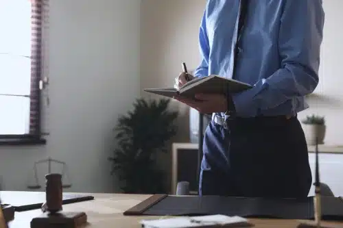 A lawyer standing up in his office and taking notes from a law book for a case.
