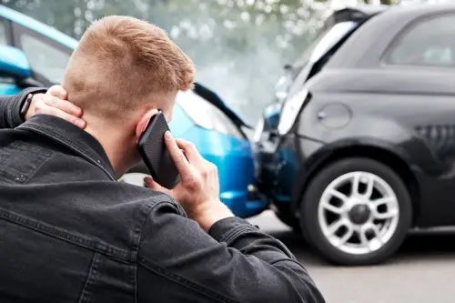A driver on a phone calling for help after a collision between his car and a black hatchback.
