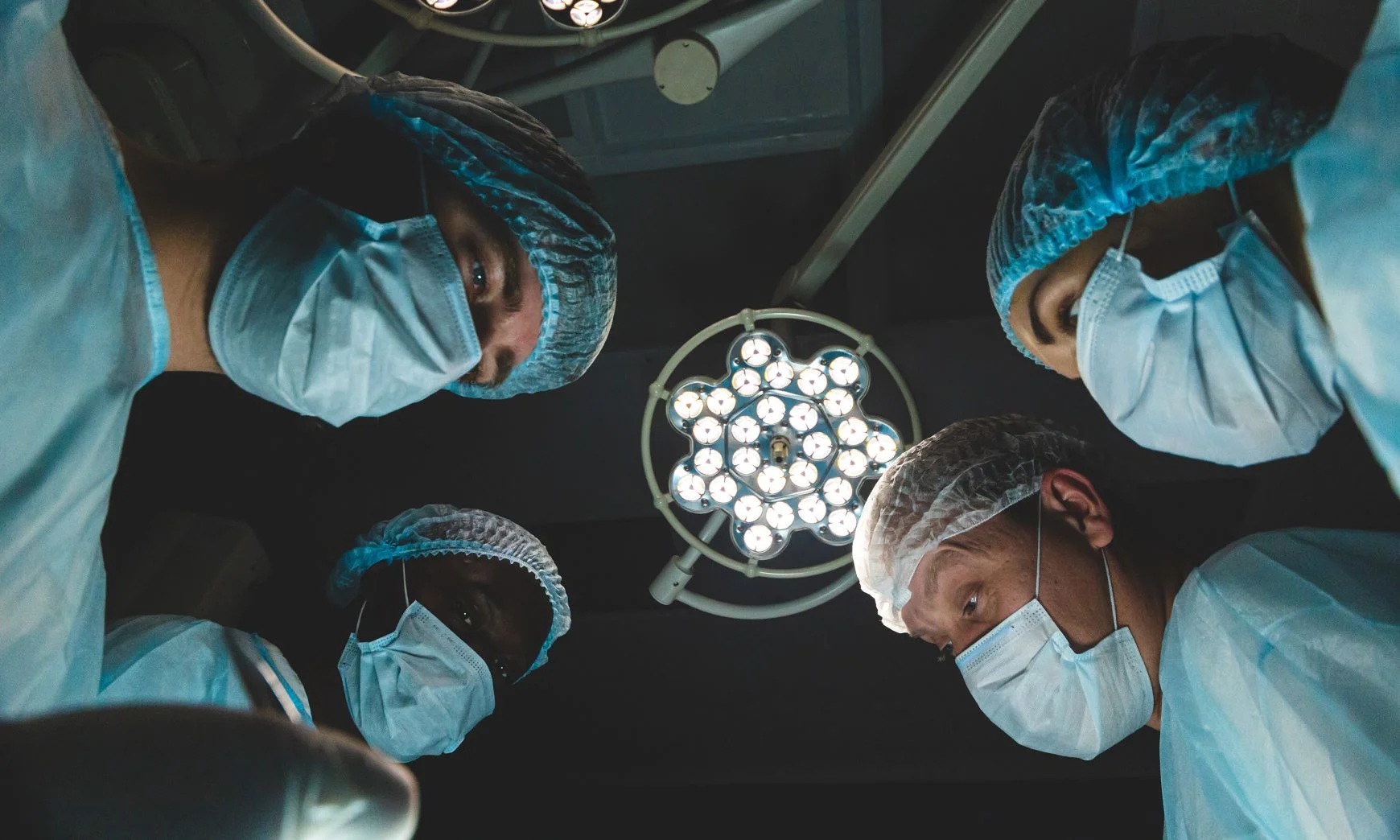 A team of doctors and nurses gathered around the viewer in an operating theater.