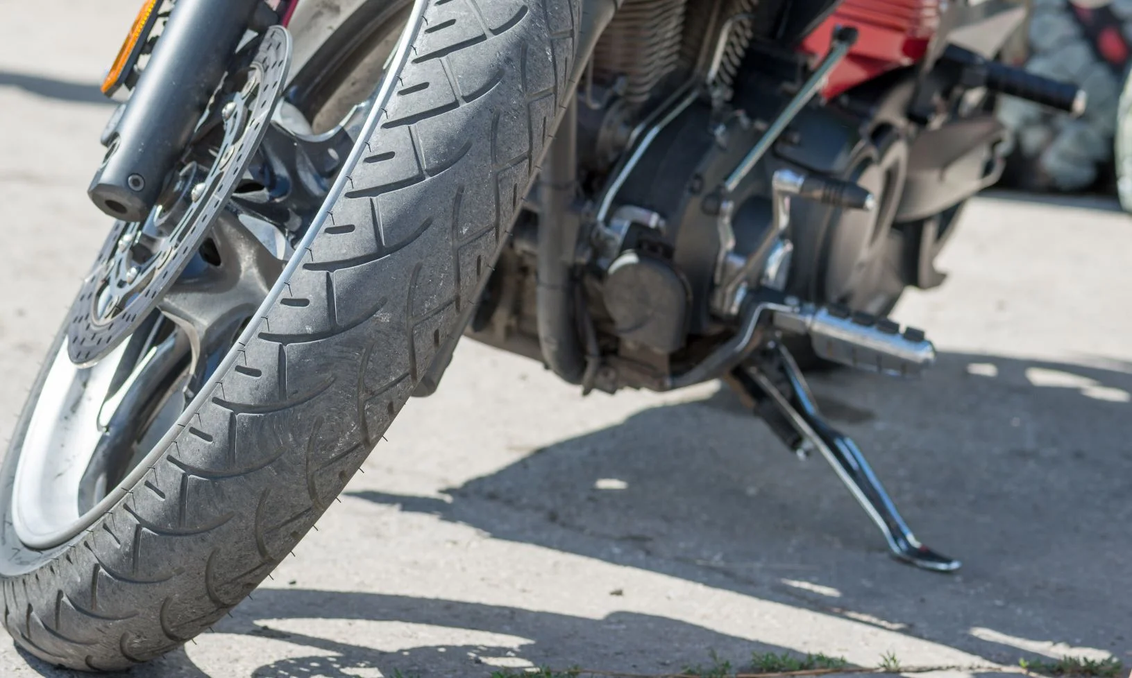 A closeup of a the front wheel of a motorcycle parked on the side of a road.
