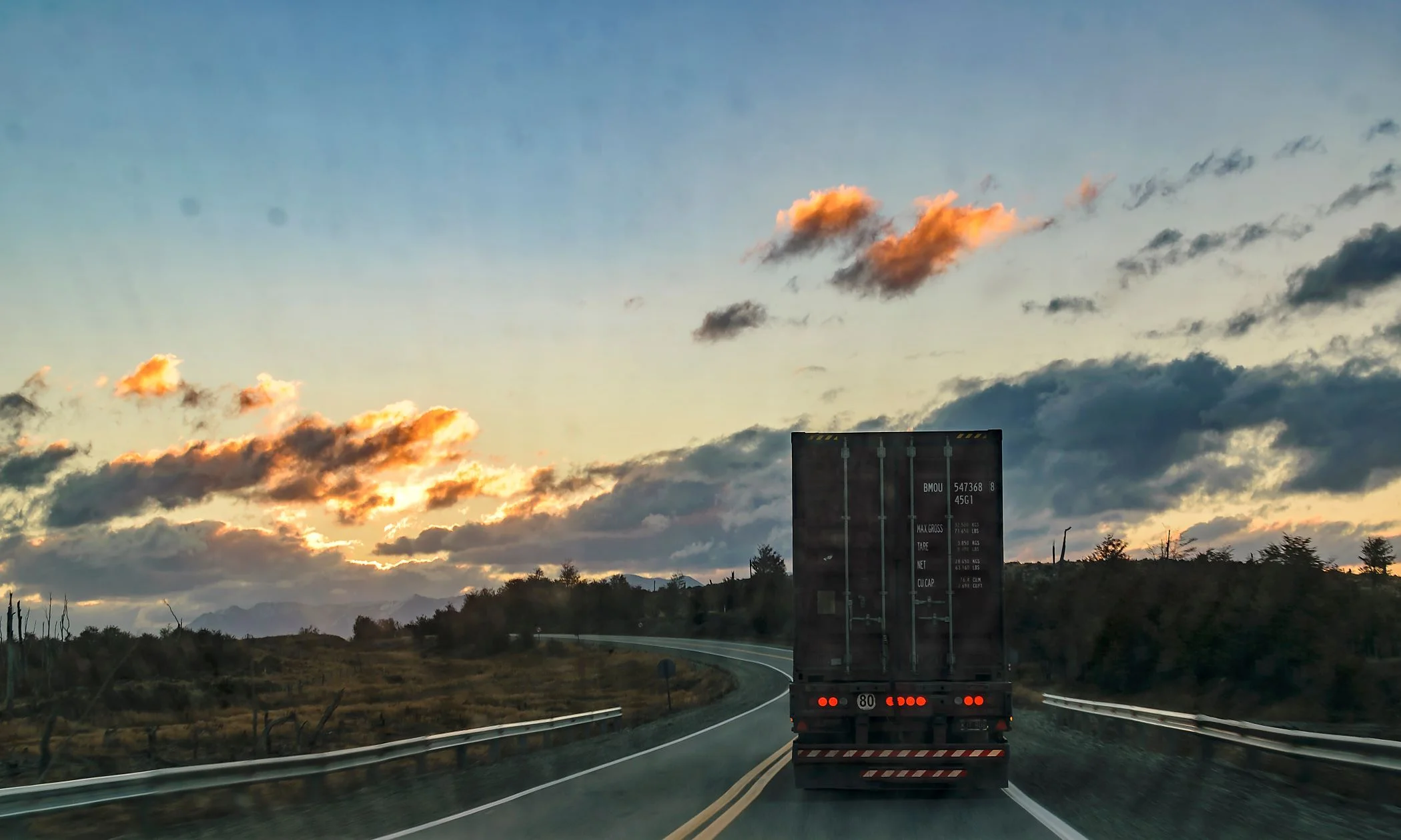 A transport truck driving along a hightway during sunset.