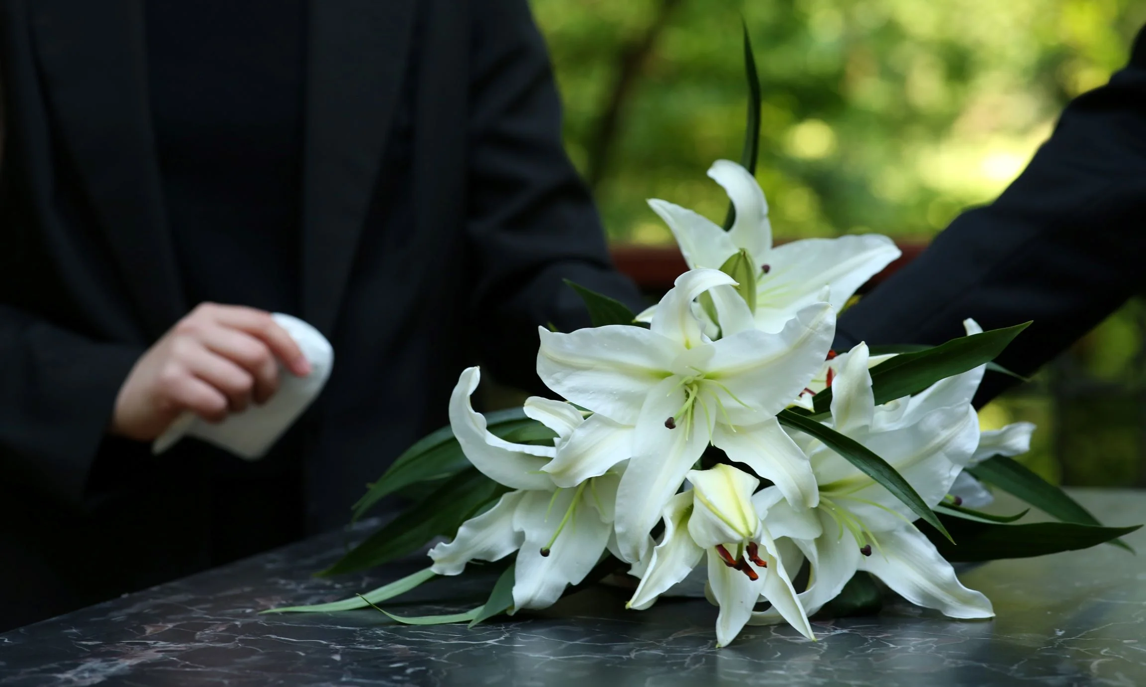 White flowers on top of an accident victim's casket with loved ones gathered around.