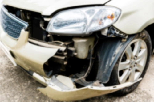 A dull-colored car's front end with the bumper and hood damaged in an accident.