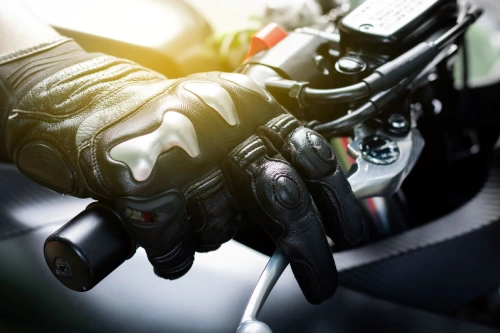 A closeup of a motorcyclist's gloved hand with fingers on the brake lever.
