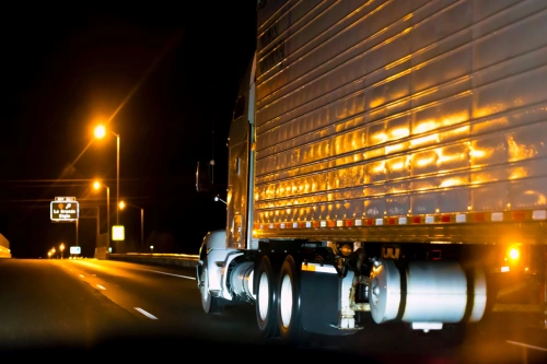 A large truck driving on a major highway at night lit by streetlights.