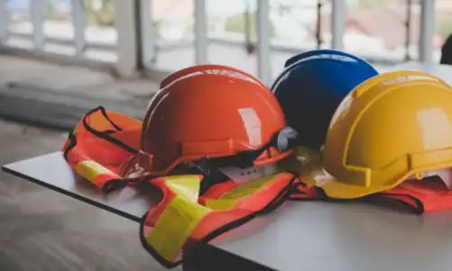 Safety vests and three hard hats of different colors on top of a table at a construction site.