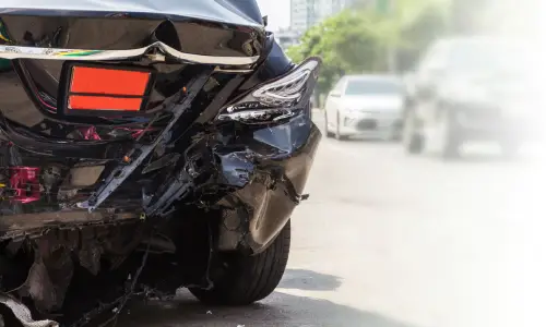 A black car on a city road after a hit and run accident where the other driver is nowhere to be seen.