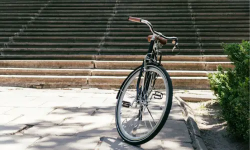 A bicycle standing in the shade next to plants at the bottom of stairs in a park.