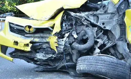 A totaled yellow vehicle in the middle of the road after a DUI car crashed into it.