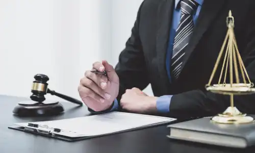 A construction accident lawyer seated at a desk with a gavel and scales and holding a pen.