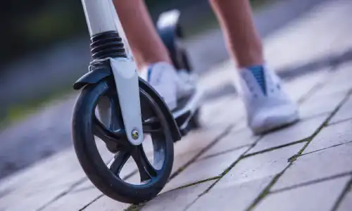 A closeup of the shoes of a girl taking a break after riding her electric scooter in a park.