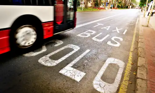 A motion-blurred New York City bus coming up to a bus stop at daytime.