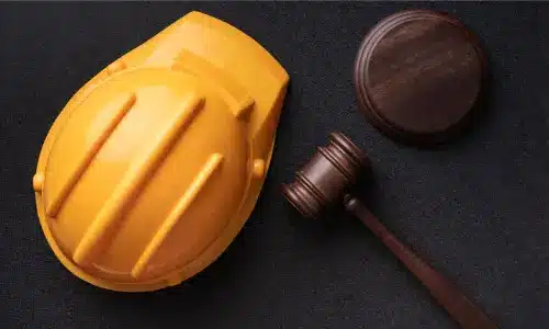 An overhead view of a gavel, soundblock, and construction safety helmet on a table.