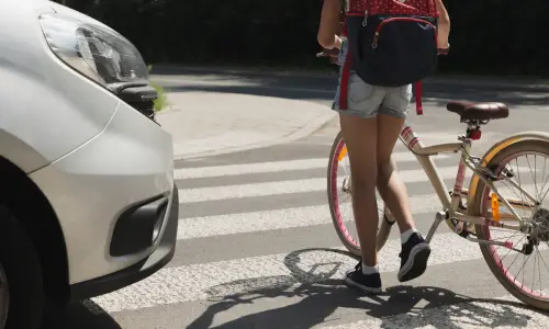 A silver-grey car stopping in time to avoid a collision with a girl walking her bicycle across a road.