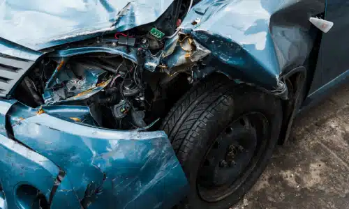 A closeup of a blue car with one of its headlights missing after a hit and run by another vehicle.