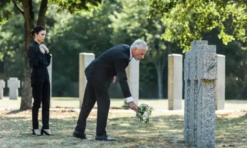 A mourning man and woman leaving a bouquet of flowers at a gravestone.