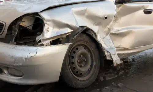 A grey car with a dented driver's side caused by a hit and run accident.