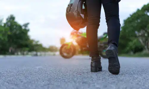 A closeup of a motorcyclist's legs as he walks toward his motorbike.