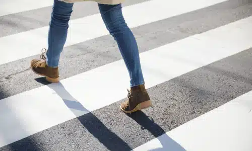 A female pedestrian walking at a brisk pace across a road at a crosswalk.