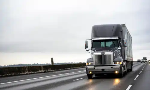 A truck driving along a straight highway on a cloudy afternoon.