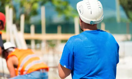 A consturction worker watching his coworker from behind while building a house.