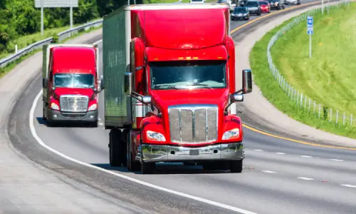 A couple of red trucks traveling on an interstate highway ahead of traffic in the background.