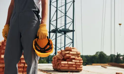 A construction worker holding a safety helmet in his hand and standing in a construction site.