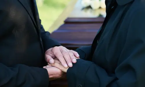 Two people holding hands and mourning at the funeral of a wrongful death victim.