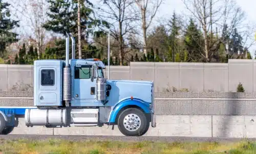 A blue semi truck driving along a highway next to a wall.