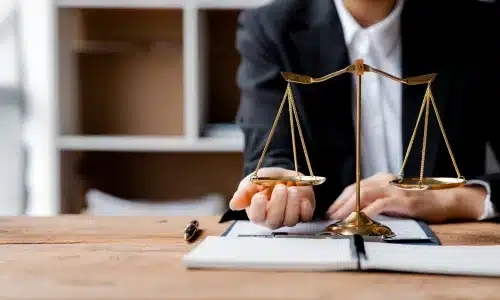 A lawyer resting his left arm on his desk while his right hand supports one pan of a scale of justice.