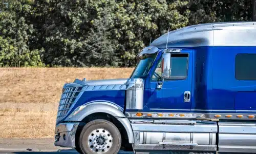 A side view shot of a blue semi truck driving along a highway.