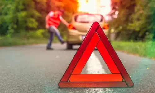 An early warning device deployed on a road with a damaged car in the background after an uninsured motorist accident.