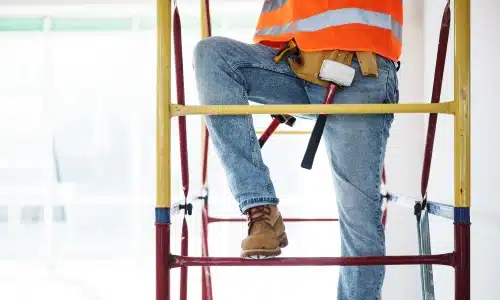 A hardhat worker climbing up a scaffolding at a construction site.