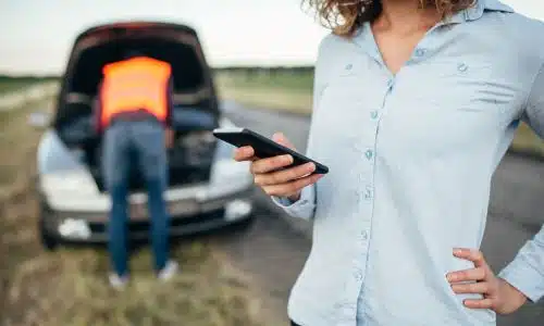 A woman contacting a lawyer on her phone while waiting for her car to be repaired after an accident.