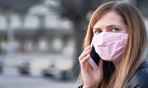 A woman wearing a mask while speaking on the phone, likely discussing joining the BioLab class action lawsuit for chemical fire impacts.