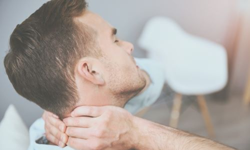 A man holding the back of his neck, appearing to experience pain or discomfort after a rideshare injury. He is sitting in a relaxed environment, suggesting possible injury or strain.