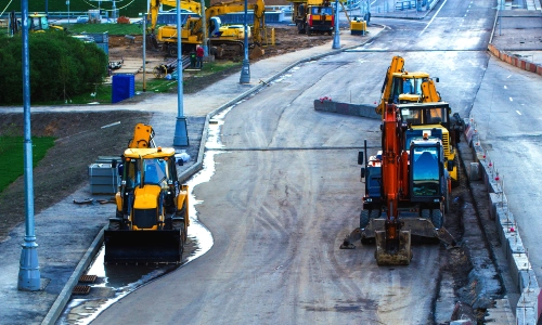 Construction vehicles doing work on a roadway in the early morning.