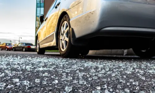 A low shot of a car on a road with shattered glass around it from a hit and run accident.