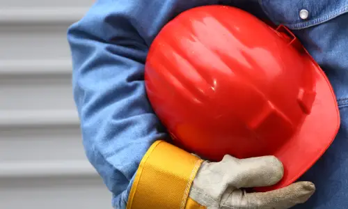 A chest level shot of a hardhat worker holding his helmet under his arm and close to his chest.