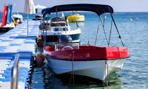 A boat docked at a long pier next to others on a bright sunny day.